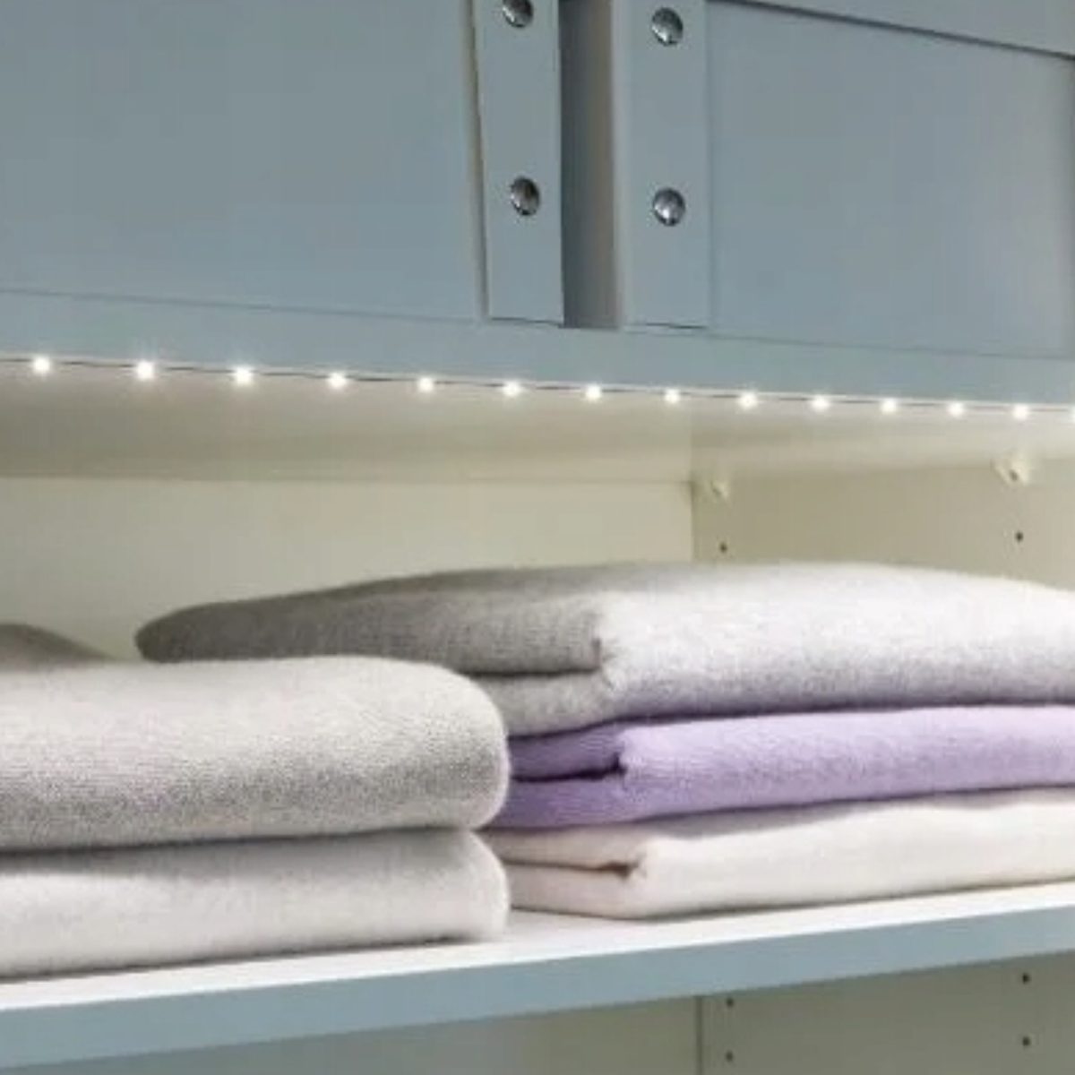 Striscia LED Livarno installata sotto pensile armadio, illuminazione ripiano con maglioni piegati