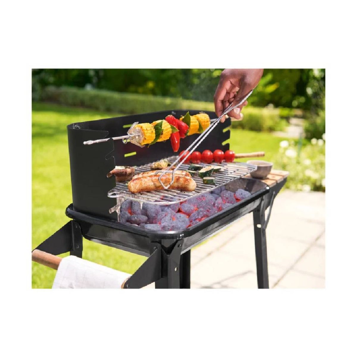 Grillmeister KANSAS in uso all'aperto durante la cottura di spiedini, salsicce e verdure sulla brace