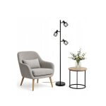 Lampada da terra Livarno Loft nera con base rotonda, ambientata in salotto con poltrona grigia e tavolino