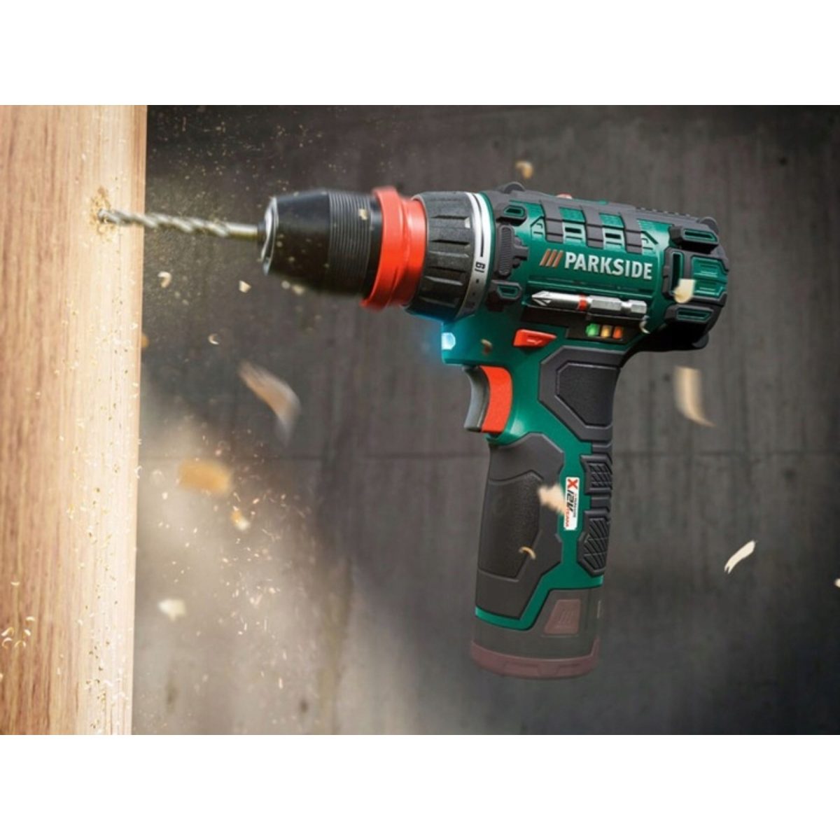Parkside Trapano Avvitatore PBSA 12 in azione mentre fora un pannello di legno con trucioli in movimento