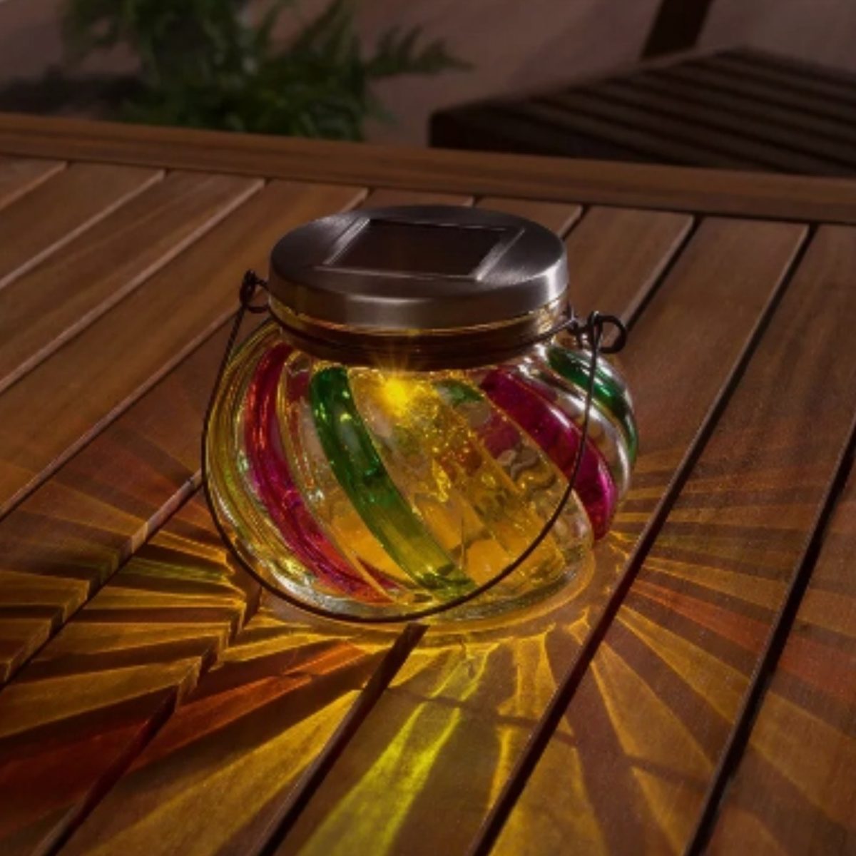 Lanterna solare Livarno Home accesa di sera su tavolo in legno da giardino, luce led calda diffusa