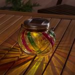 Lanterna solare Livarno Home accesa di sera su tavolo in legno da giardino, luce led calda diffusa