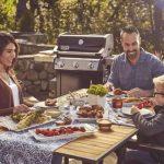 Famiglia riunita a tavola con barbecue Weber Spirit E-315 GBS in giardino durante un pranzo estivo
