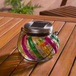 Lanterna solare Livarno Home in vetro colorato spenta su tavolo da giardino, dettaglio pannello solare e vetro decorato